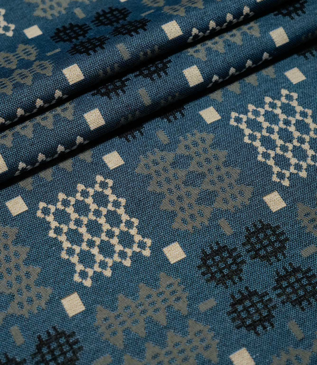 Kinfolk fabric arranged in soft folds, showing its terracotta orange ground and repeating geometric pattern.