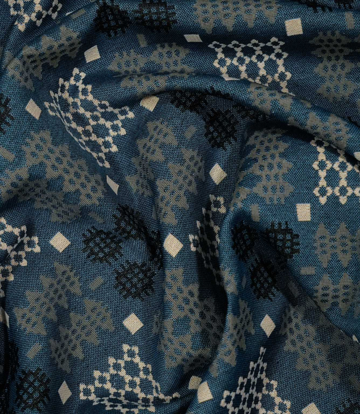 A close-up of draped fabric with a woven geometric pattern in slate blue, beige, and black.