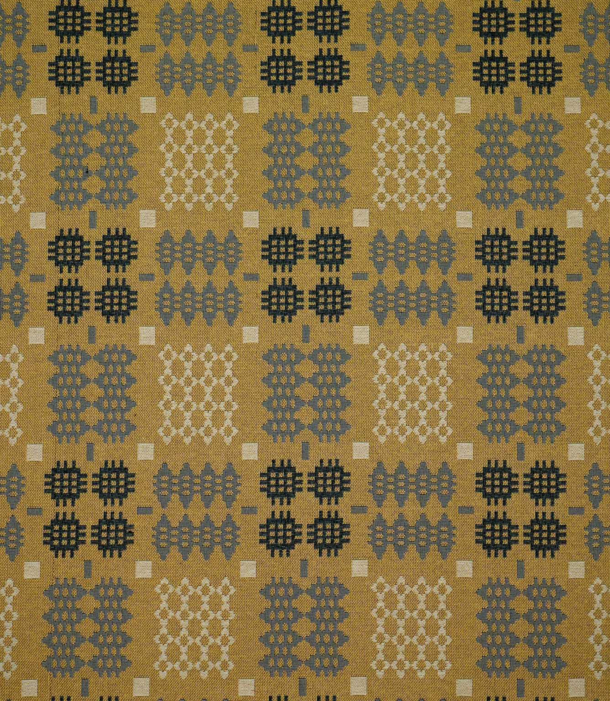 Kinfolk geometric fabric shown flat, with a mustard yellow ground and repeating charcoal, grey and cream woven motifs arranged in a structured pattern.