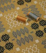 Kinfolk geometric fabric with mustard and grey thread spools placed on top, showing the woven texture and contrasting grey, charcoal and cream pattern.