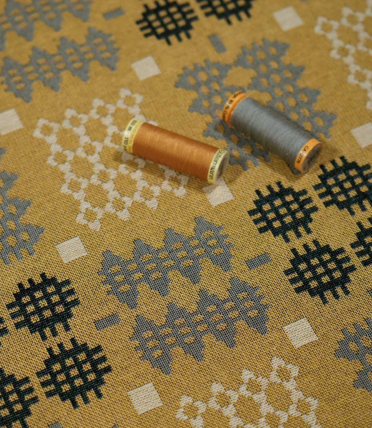 Kinfolk geometric fabric with mustard and grey thread spools placed on top, showing the woven texture and contrasting grey, charcoal and cream pattern.