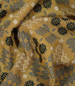 Draped Kinfolk geometric fabric showing how the material falls, with a textured mustard yellow ground and repeating charcoal, grey and cream motifs.