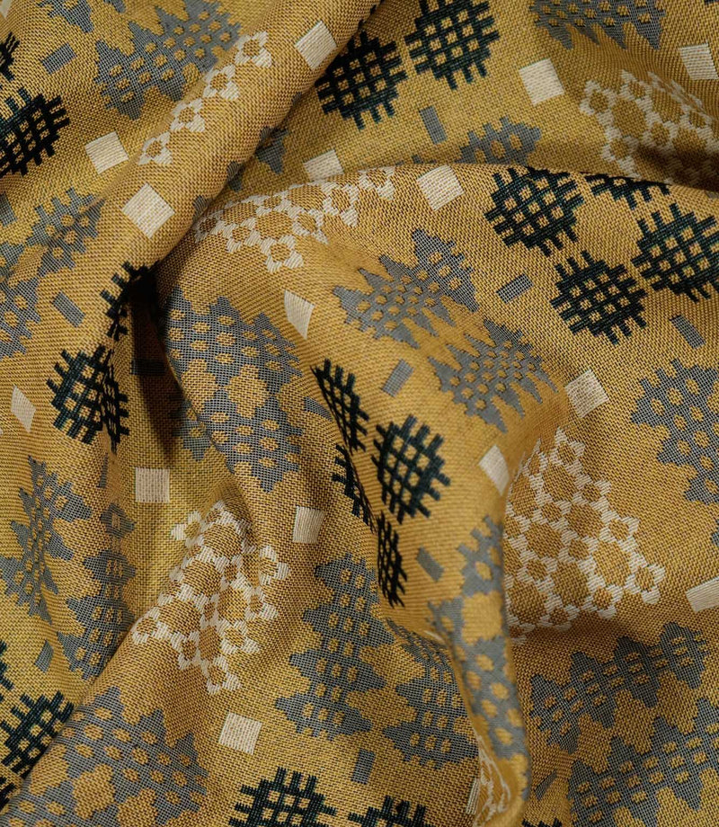 Draped Kinfolk geometric fabric showing how the material falls, with a textured mustard yellow ground and repeating charcoal, grey and cream motifs.