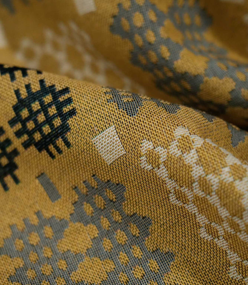 Macro close-up of Kinfolk fabric in mustard yellow, showing the detailed woven texture and contrasting charcoal, grey and cream geometric motifs.