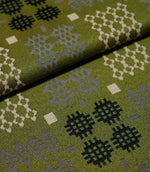 Folded Kinfolk fabric showing the scale and detail of its geometric design, with black, grey and cream motifs on an olive green ground.