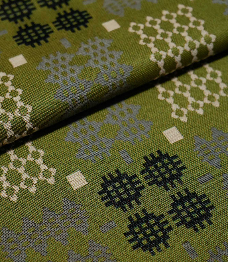 Folded Kinfolk fabric showing the scale and detail of its geometric design, with black, grey and cream motifs on an olive green ground.