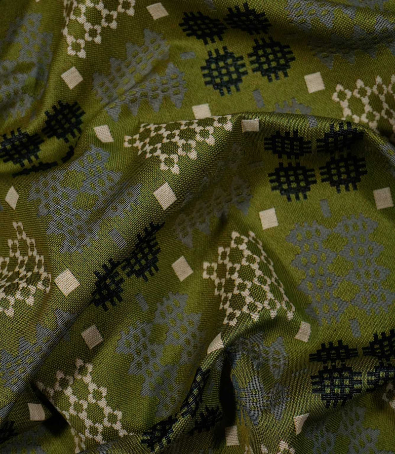 Draped Kinfolk geometric fabric showing how the material falls into soft folds, with an olive green ground and repeating black, grey and cream woven-style motifs.