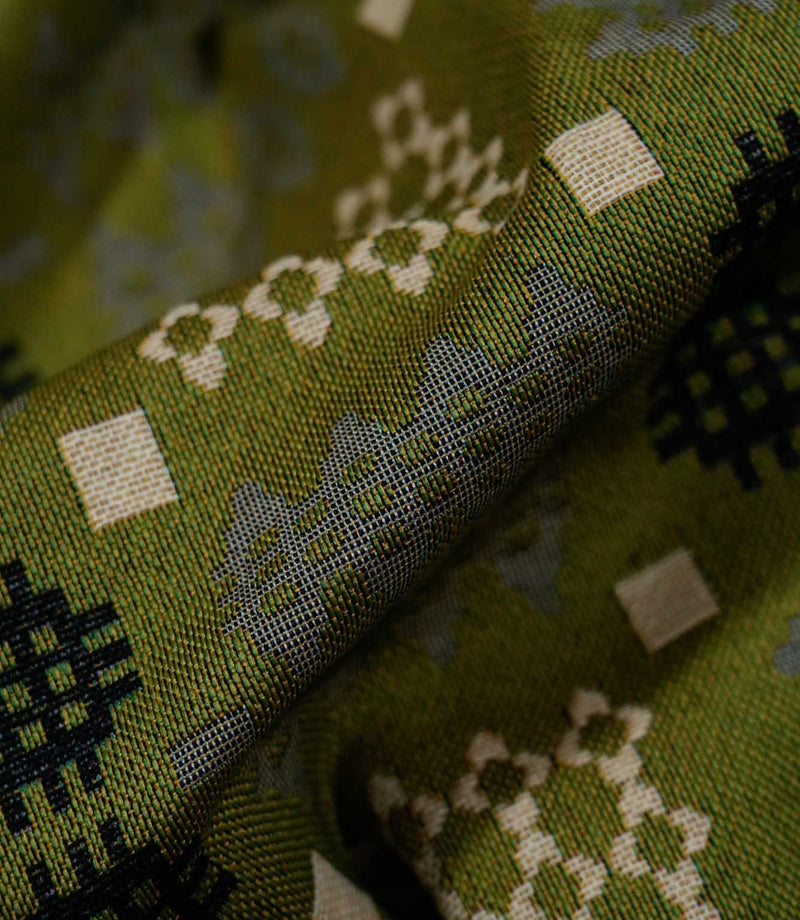 Macro close-up of Kinfolk fabric showing the detailed woven texture and geometric grey, black and cream motifs against an olive green ground.