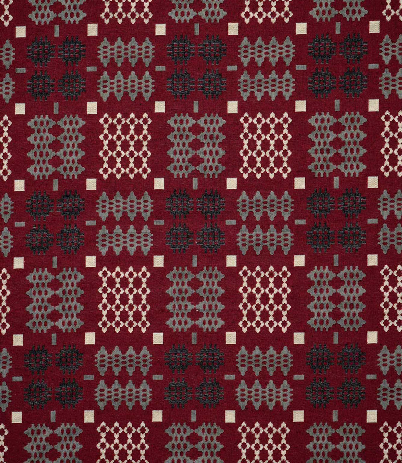 Kinfolk geometric fabric shown flat, featuring a rich red ground with repeating black, soft grey and cream woven-style motifs in a structured pattern.