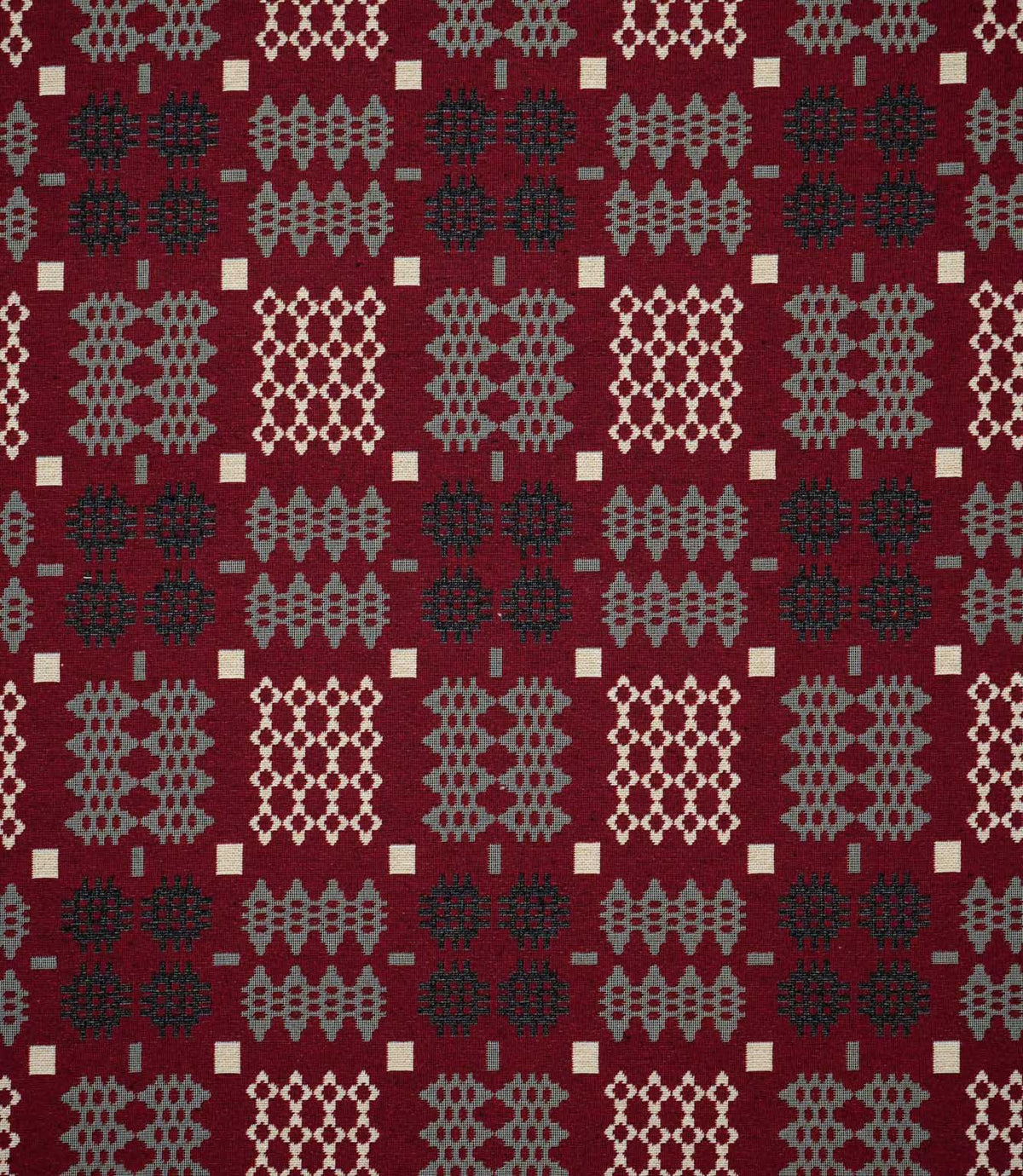 Kinfolk geometric fabric shown flat, featuring a rich red ground with repeating black, soft grey and cream woven-style motifs in a structured pattern.
