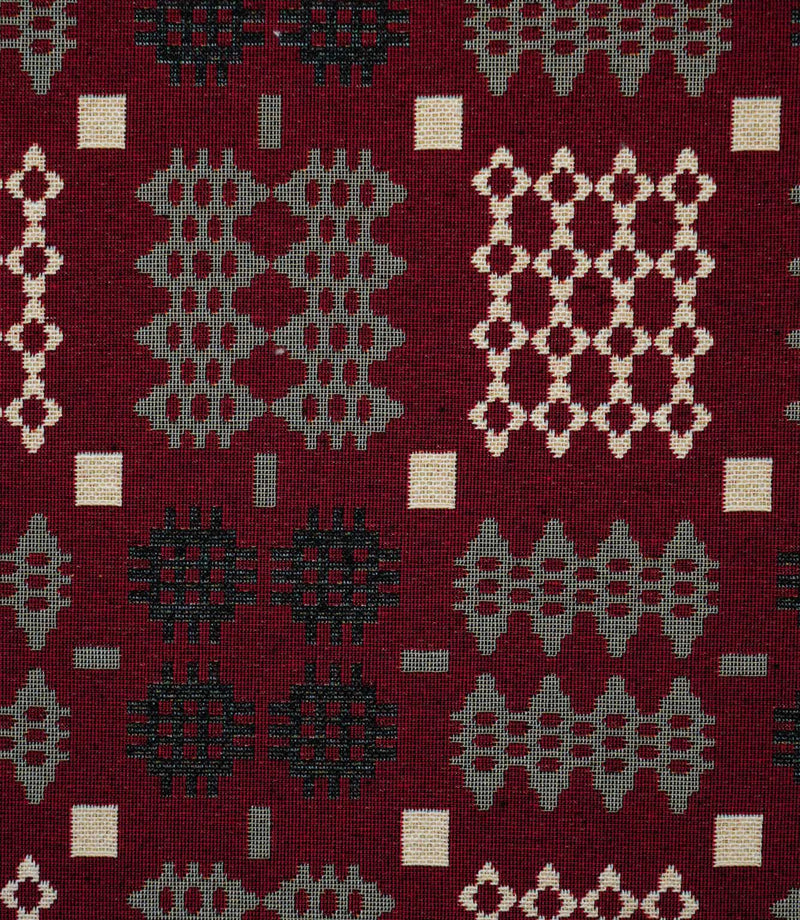 Close-up of Kinfolk fabric showing the textured weave and geometric pattern in black, grey and cream against a deep red background.