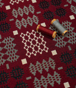 Kinfolk geometric fabric with red and grey thread spools resting on the surface, highlighting the woven texture and contrasting cream, grey and black motifs.