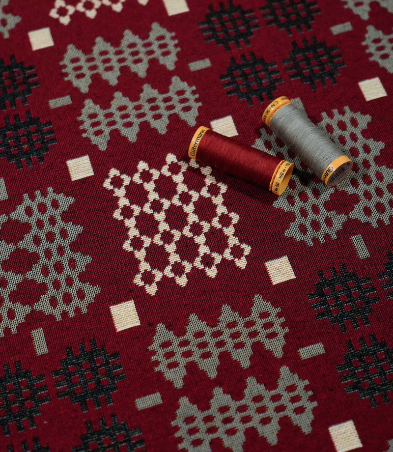 Kinfolk geometric fabric with red and grey thread spools resting on the surface, highlighting the woven texture and contrasting cream, grey and black motifs.