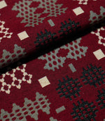 Close-up of folded Kinfolk fabric, showing the scale and woven detail of its black, grey and cream geometric motifs on a rich red ground.