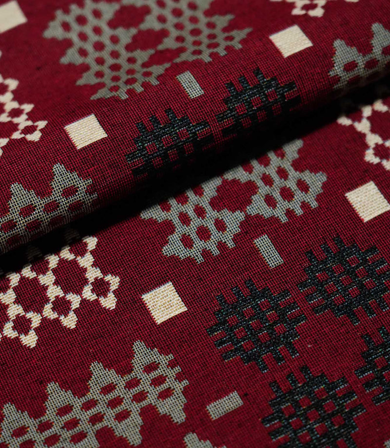 Close-up of folded Kinfolk fabric, showing the scale and woven detail of its black, grey and cream geometric motifs on a rich red ground.