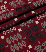 Kinfolk fabric arranged in neat folds, displaying repeating geometric motifs in black, soft grey and cream against a textured deep red background.