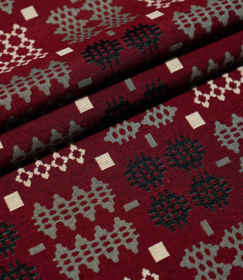 Kinfolk fabric arranged in neat folds, displaying repeating geometric motifs in black, soft grey and cream against a textured deep red background.