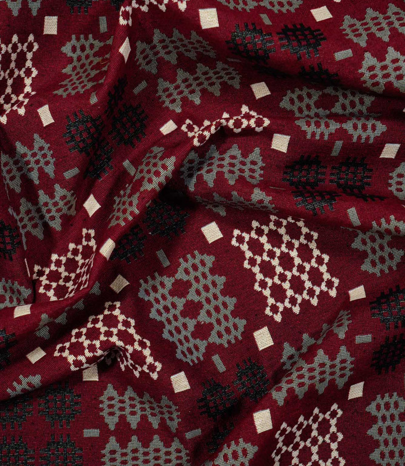 Draped Kinfolk geometric fabric showing its soft folds and repeating black, grey and cream woven-style pattern on a rich red ground.