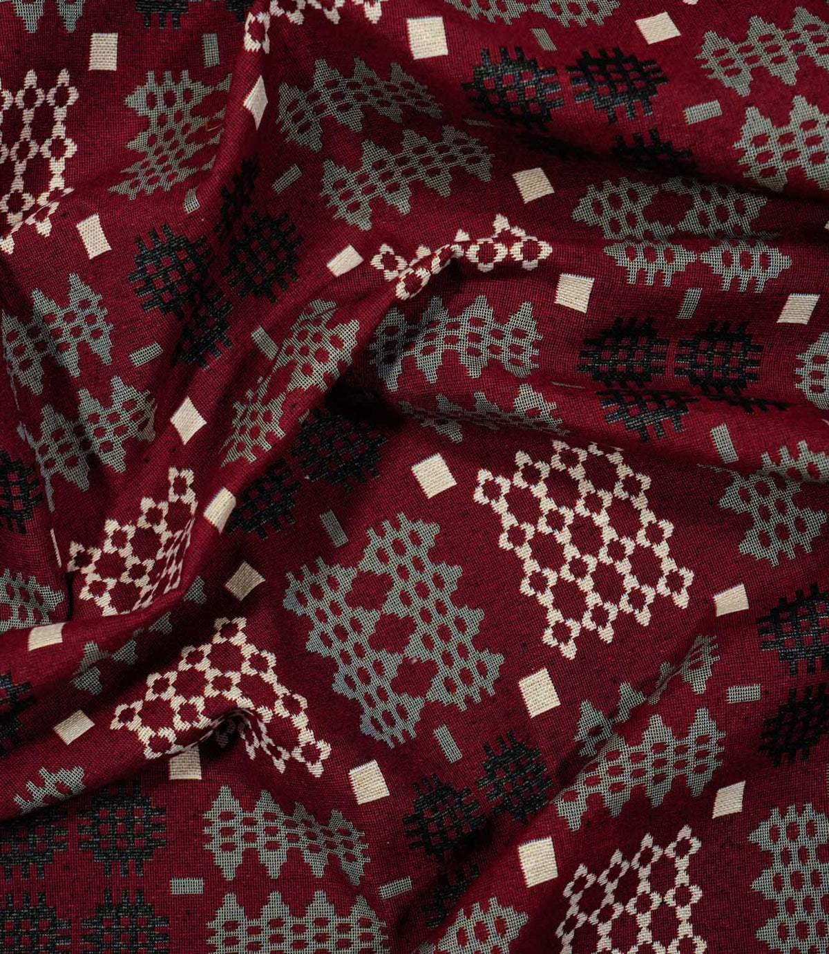 Draped Kinfolk geometric fabric showing its soft folds and repeating black, grey and cream woven-style pattern on a rich red ground.