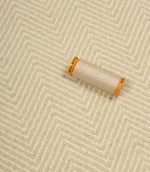 Close-up of a spool of beige thread on a textured fabric background with a herringbone pattern.