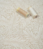 Larkspur Linen Look floral fabric with cream and beige thread spools resting on the surface, showing the scale and detail of the botanical pattern.