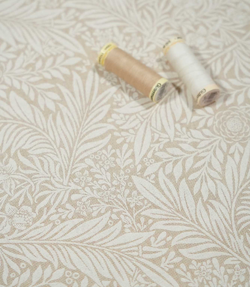 Larkspur Linen Look floral fabric with cream and beige thread spools resting on the surface, showing the scale and detail of the botanical pattern.