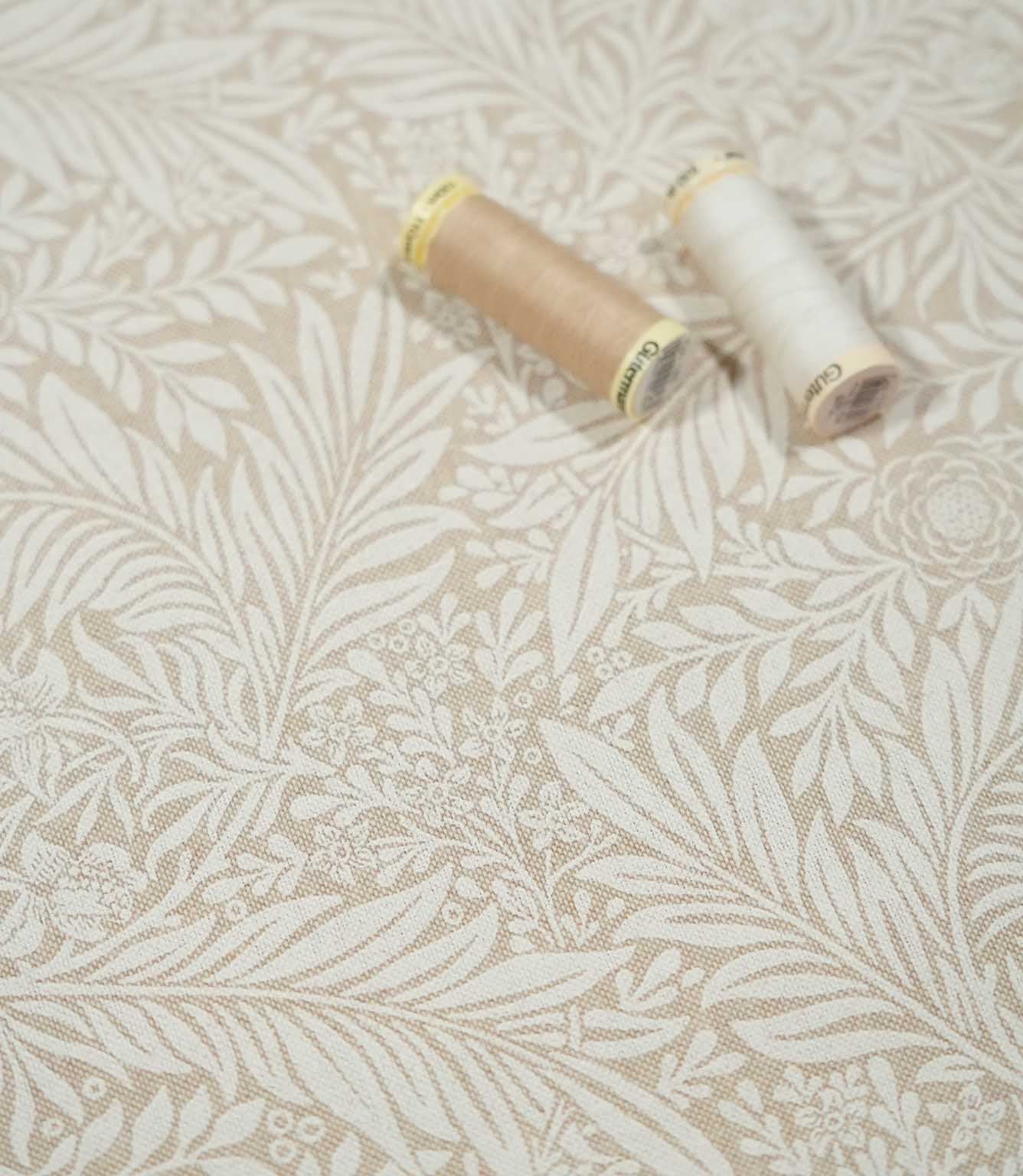 Larkspur Linen Look floral fabric with cream and beige thread spools resting on the surface, showing the scale and detail of the botanical pattern.