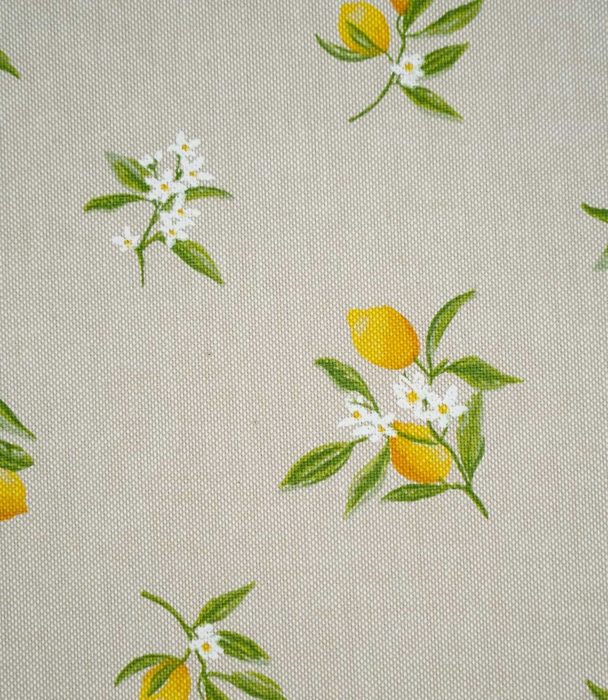 Close-up of Lemon Grove Natural fabric showing small yellow lemons, detailed green foliage and white citrus blossoms with yellow centres on a textured beige woven surface.