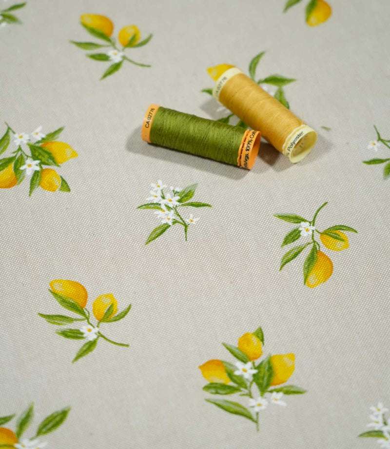 Lemon Grove Natural citrus print fabric photographed with green and yellow sewing thread spools for scale, highlighting the small-scale lemon motifs, white blossoms and natural woven texture.