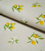 Lemon Grove Natural fabric folded over itself, showing the scattered yellow lemon print, fresh green leaves and delicate white citrus flowers on a natural beige background.