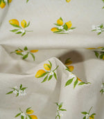 Lemon Grove Natural fabric loosely draped into soft folds, featuring small yellow lemons, delicate white citrus flowers and green leaves against a natural beige woven background.