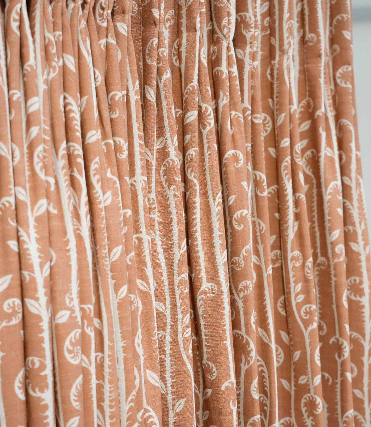 Little Bracken Rust fabric gathered into soft curtain folds, featuring an off-white botanical fern and foliage design on a warm rust orange background.