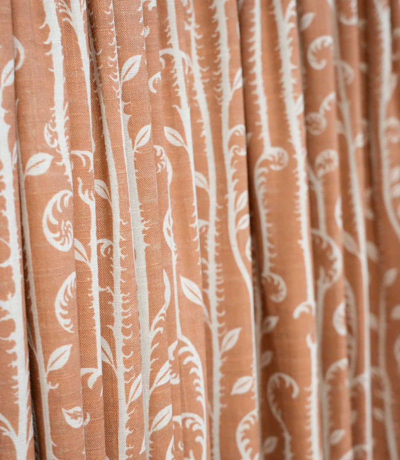Close-up of Little Bracken Rust curtain fabric showing the off-white bracken fern and leafy botanical pattern across a textured rust orange ground.