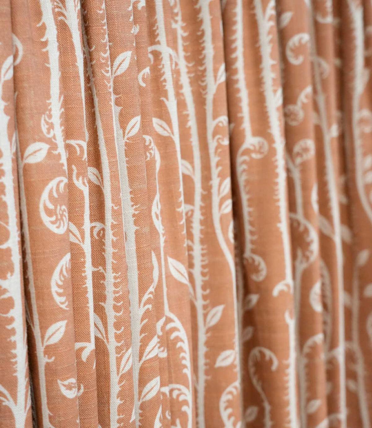 Close-up of Little Bracken Rust curtain fabric showing the off-white bracken fern and leafy botanical pattern across a textured rust orange ground.