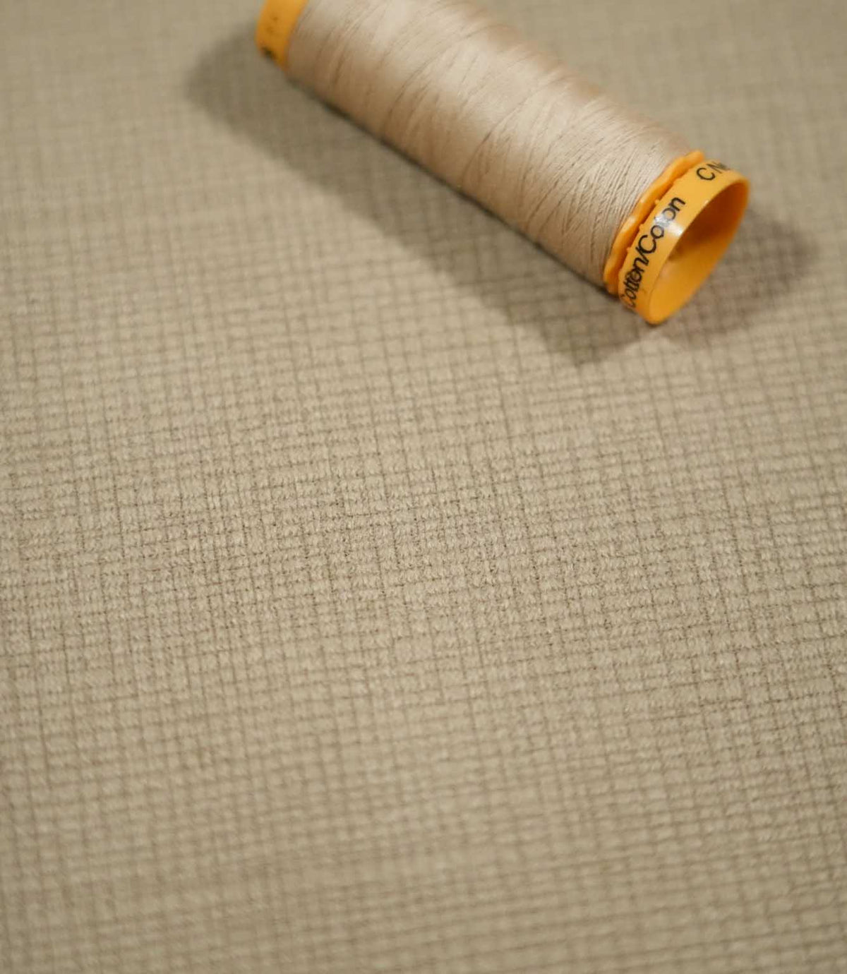 Lois Velvet Oat fabric laid flat with a coordinating beige sewing thread spool, highlighting the warm oatmeal colour, subtle crosshatched texture and fine velvet pile.