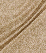 Manorville Dune floral fabric arranged in soft, flowing folds, showcasing its warm sandy beige background, delicate cream flowers and winding leafy stems, with the intricate botanical pattern continuing across the draped fabric.