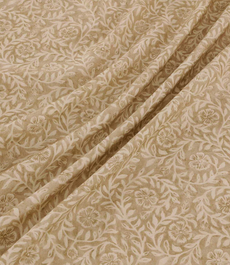 Manorville Dune floral fabric arranged in soft, flowing folds, showcasing its warm sandy beige background, delicate cream flowers and winding leafy stems, with the intricate botanical pattern continuing across the draped fabric.