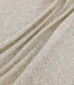 Manorville Gull floral fabric arranged in soft, flowing folds, showing its delicate ivory flowers, intertwining leafy vines and warm grey-beige background, with the botanical pattern continuing naturally across the draped material.
