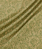 Manorville Kelp fabric arranged in soft, flowing folds, showcasing its detailed beige floral and foliage pattern against a natural moss green background, with delicate blossoms, intertwining stems and a subtly textured finish.