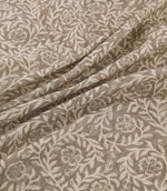 Manorville Quaker fabric arranged in soft, flowing folds, showcasing its intricate ivory floral and foliage design on a warm taupe background, with detailed blossoms, winding stems and a natural woven texture.
