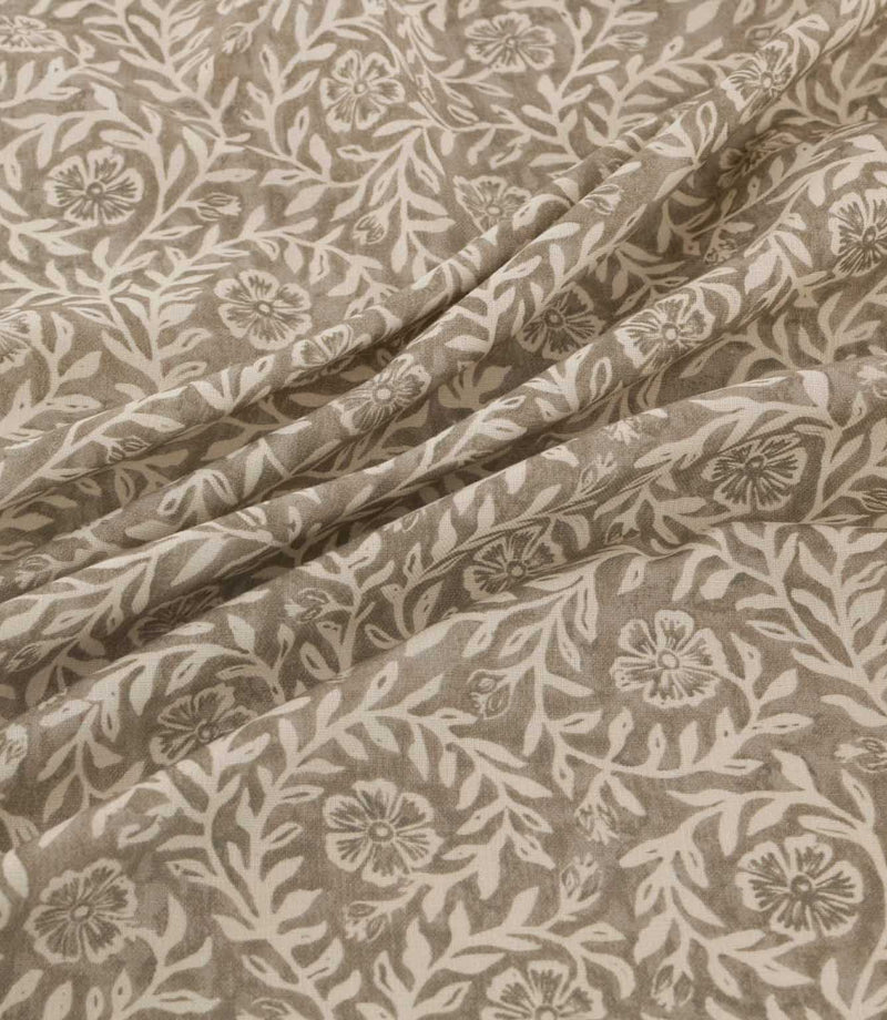 Manorville Quaker fabric arranged in soft, flowing folds, showcasing its intricate ivory floral and foliage design on a warm taupe background, with detailed blossoms, winding stems and a natural woven texture.
