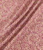Manorville Rosehip fabric arranged in soft, flowing folds, showcasing its intricate cream floral and foliage pattern against a muted rose pink background, with delicate blossoms, intertwining stems and a subtly textured finish.