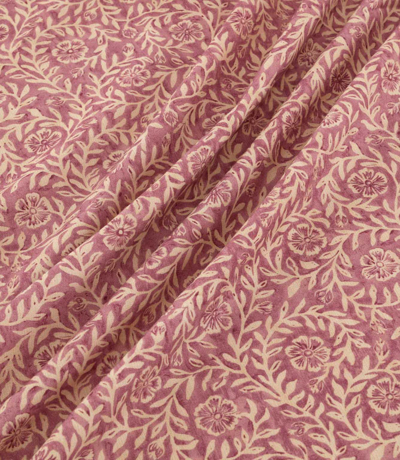 Manorville Rosehip fabric arranged in soft, flowing folds, showcasing its intricate cream floral and foliage pattern against a muted rose pink background, with delicate blossoms, intertwining stems and a subtly textured finish.