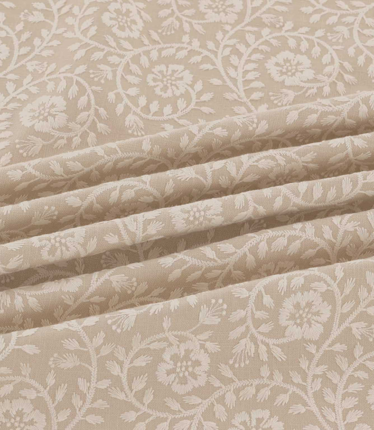 Close-up of Marion Quaker fabric draped in soft folds, highlighting the intricate ivory embroidered flowers, trailing vines and delicate foliage on a natural beige woven background.