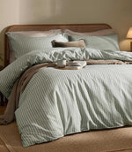 Marlow Stripe Artichoke/Sage duvet cover and matching pillowcases styled with a neutral throw, natural cane headboard and warm beige bedroom furnishings.