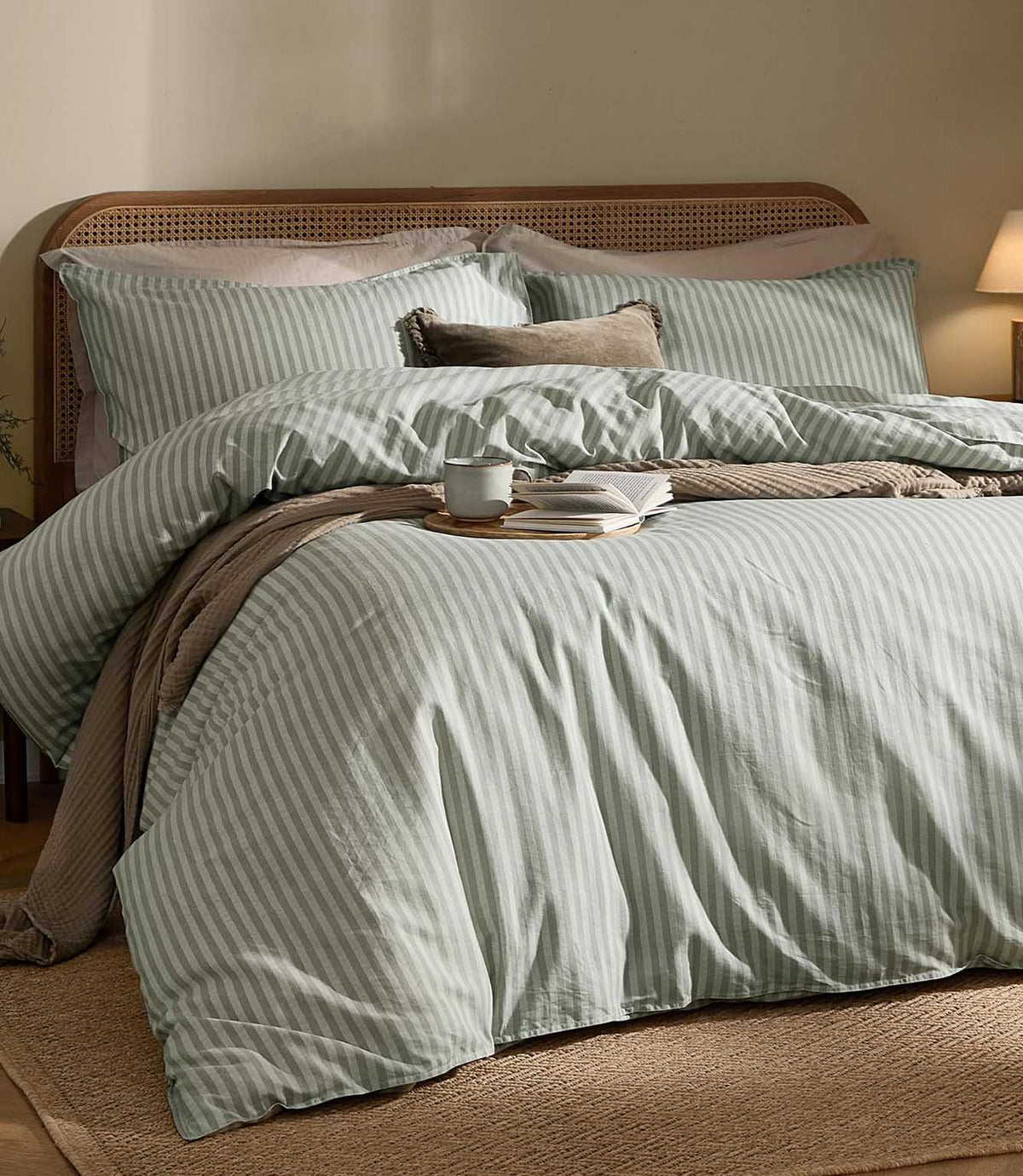 Marlow Stripe Artichoke/Sage duvet cover and matching pillowcases styled with a neutral throw, natural cane headboard and warm beige bedroom furnishings.