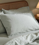 Close-up of Marlow Stripe pillowcases and duvet cover in Artichoke/Sage, showing the fine sage green and off-white striped pattern and softly relaxed fabric finish.