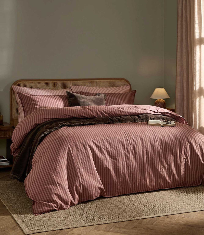 Marlow Stripe Duvet Cover Set in Chocolate/Rosewood, styled on a bed with warm rose pink and chocolate brown stripes, dark brown throw and natural cane headboard.
