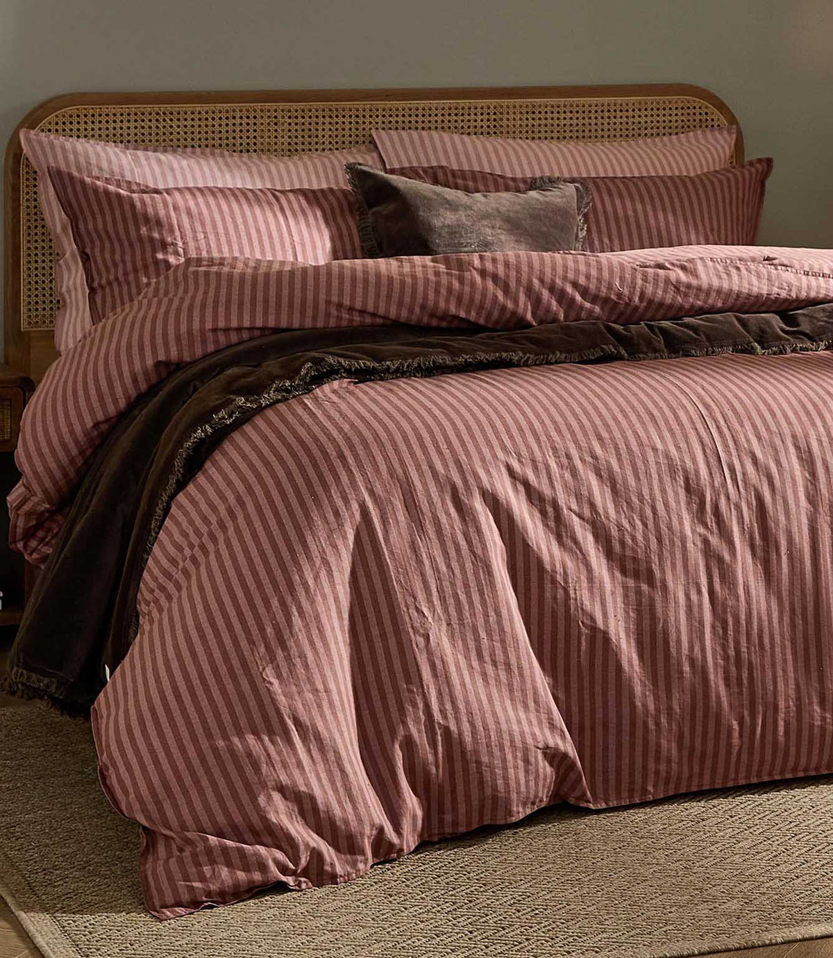 Marlow Stripe Chocolate/Rosewood duvet cover and coordinating pillowcases styled with a dark brown throw, cane headboard and warm neutral bedroom furnishings.
