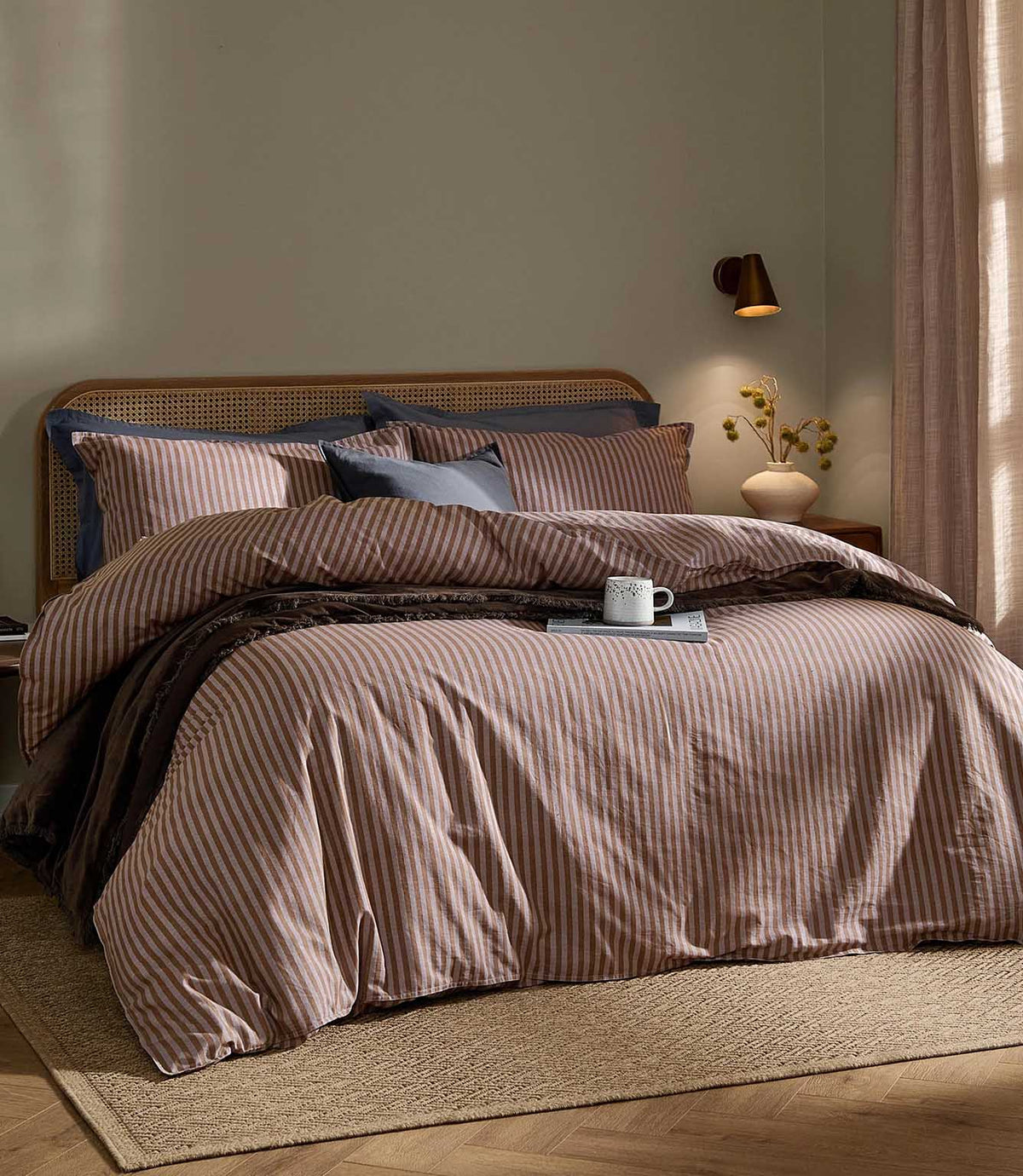 Marlow Stripe Duvet Cover Set in Cocoa/Vintage Blue styled on a bed, with cocoa brown and soft vintage blue stripes, blue cushions, a dark brown throw and cane headboard.